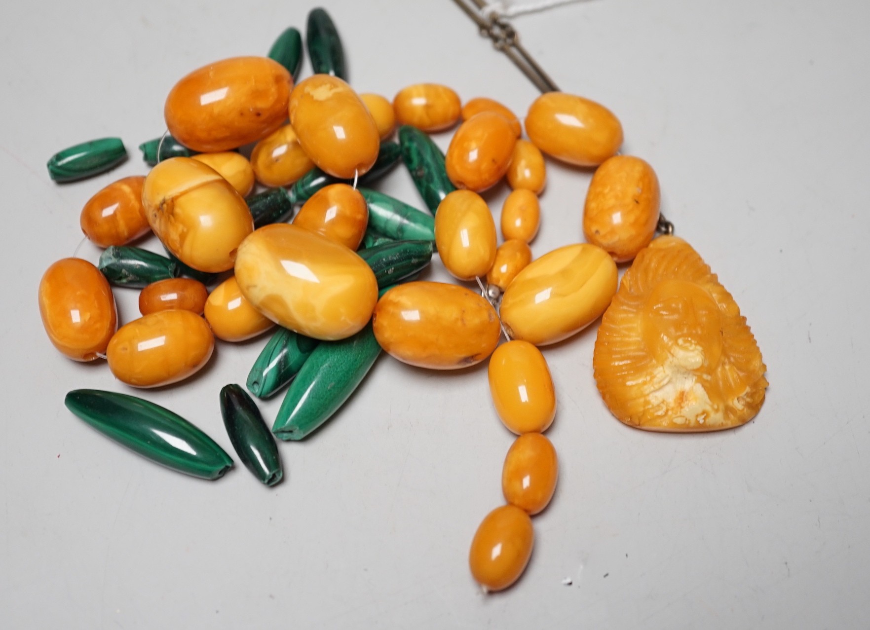 A single strand graduated amber bead necklace, a.f., 45 grams, a carved amber pendant on chain and assorted malachite beads.